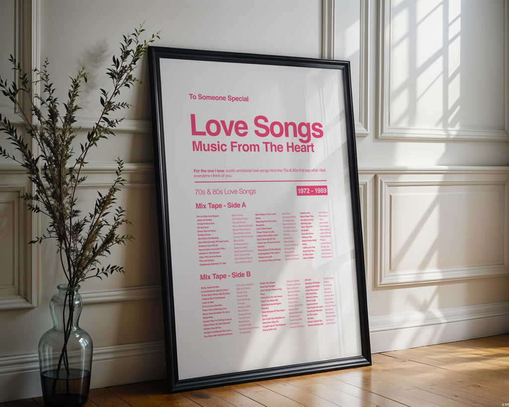 Framed poster titled 'Love Songs Music From The Heart' on a wall with a vase and plant in the foreground.