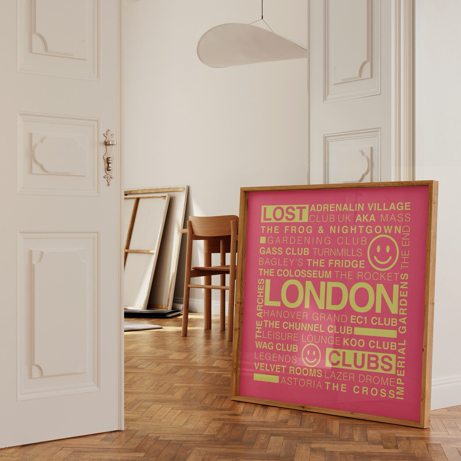 Lost London Clubs square music print with electric pink background and acid yellow text in a wooden frame leaning against a white ornate wall