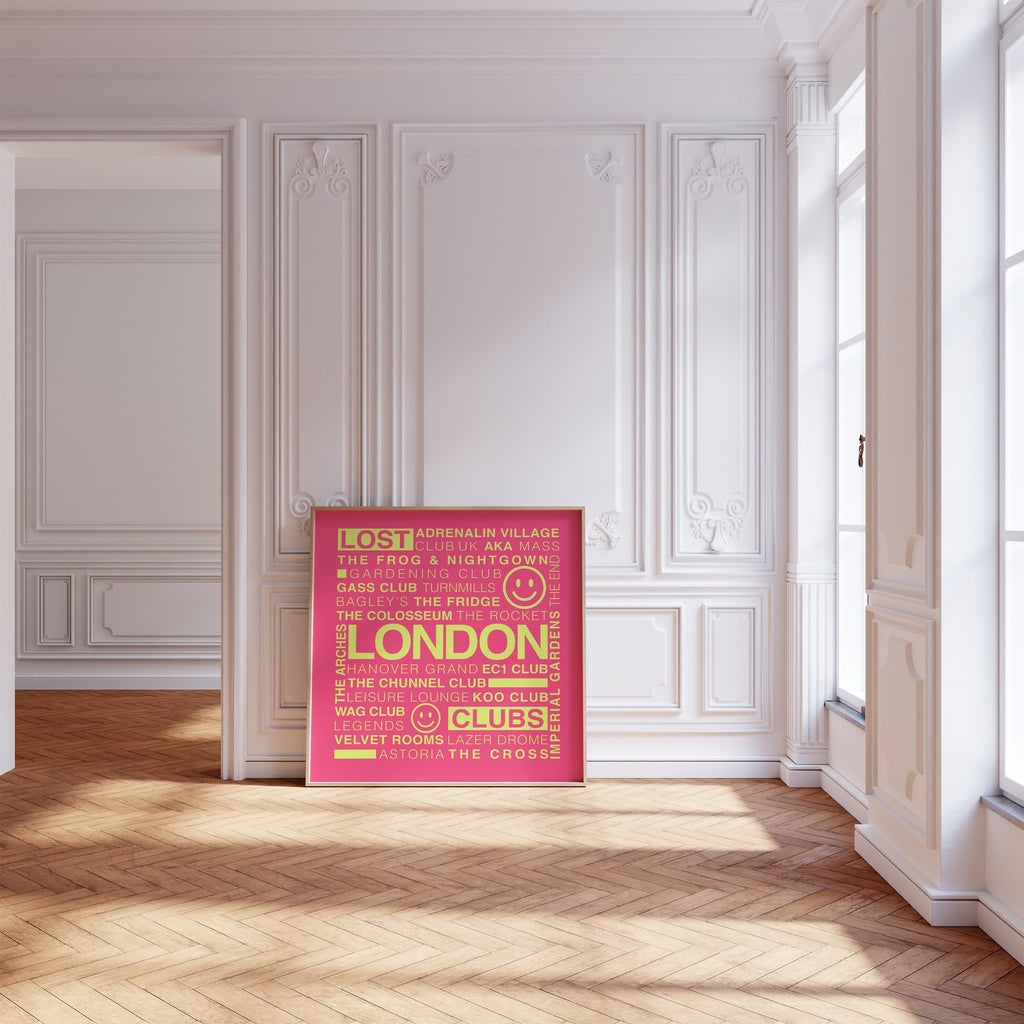 Lost London Clubs square print with electric pink background and acid yellow text displayed in a wooden frame leaning on a wood floor against a white ornate wall