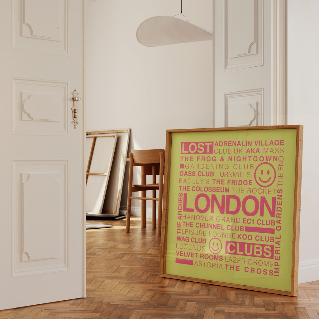 Lost London Clubs square music print with electric pink text on acid yellow in a wooden frame leaning against a white ornate wall