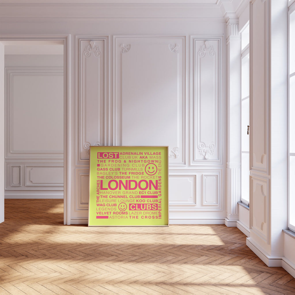 Lost London Clubs square print with electric pink text on acid yellow displayed in a wooden frame leaning on a wood floor against a white ornate wall