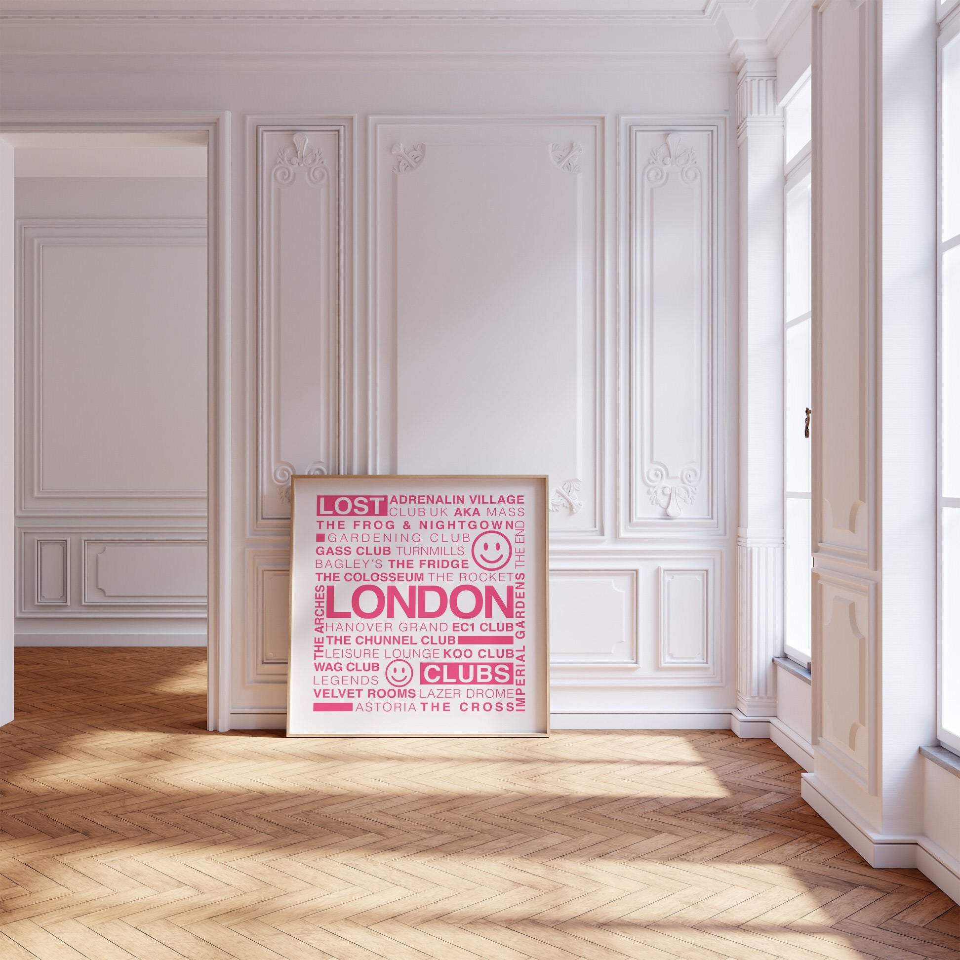 Lost London Clubs square print with electric pink text on white displayed in a wooden frame leaning on a wood floor against a white ornate wall and large windows