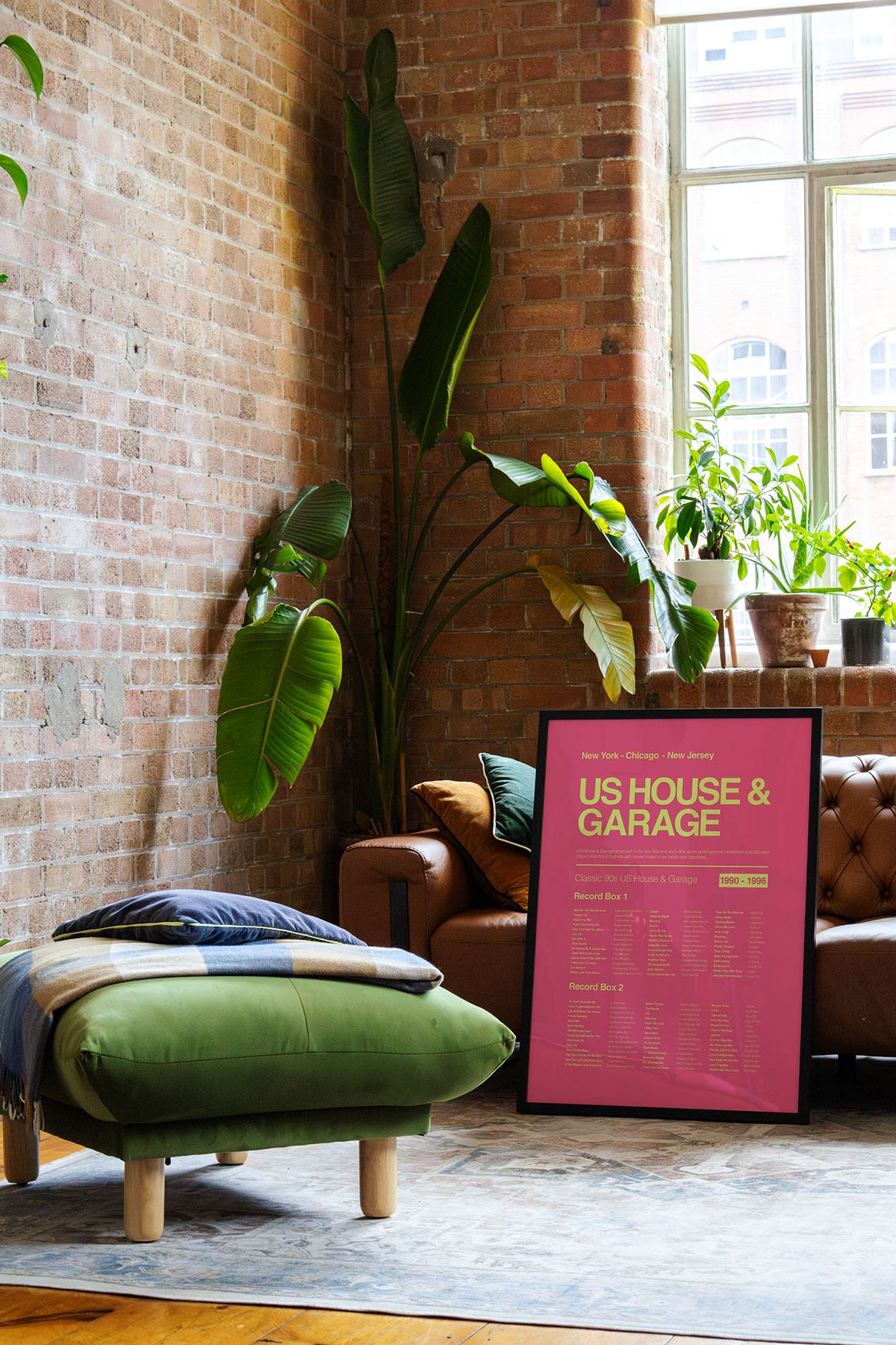 US House & Garage music print in a black frame resting on a leather sofa in a natural light-filled brick loft with warm reflective lighting. Suitable for A1, A2 and A3 sizes. Electric pink background with acid yellow text (Mockup M12).